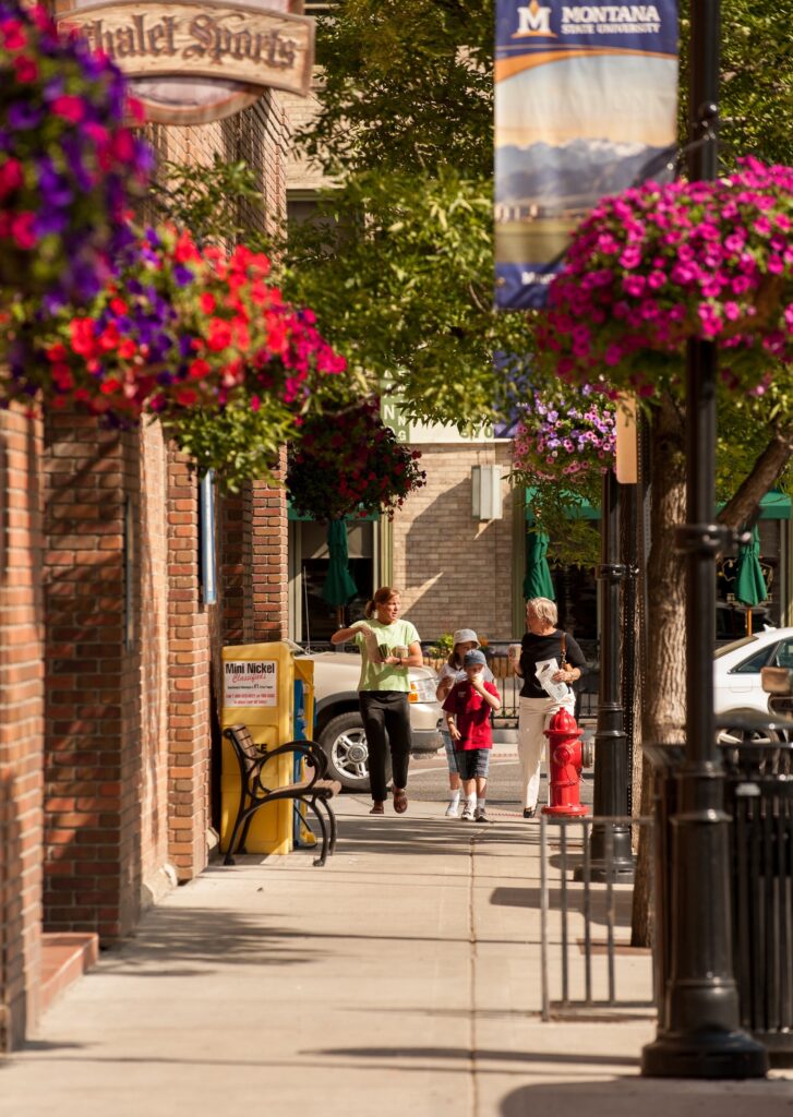 Hanging flower baskets and pedestrians along the sidewalk in downtown Bozeman, Montana, in summer