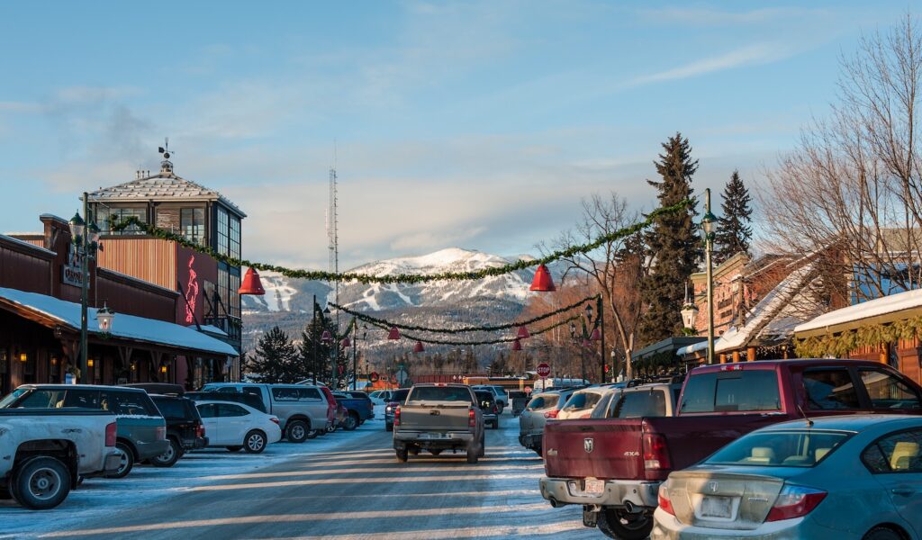 Central Avenue in downtown Whitefish in winter, with holiday garlands and red bells and Whitefish Mountain's ski runs beyond