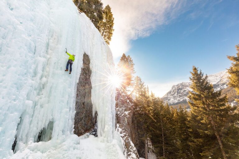 Ice climber on a frozen waterfall in Hyalite Canyon near Bozeman, Montana, with sun over snowy peaks