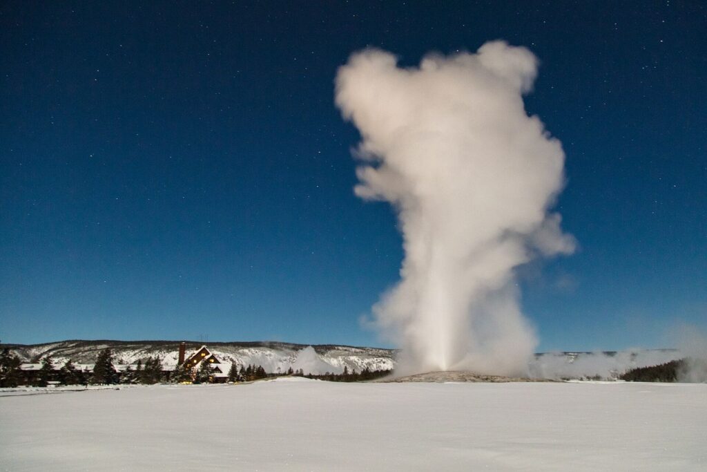 Old Faithful geyser erupting under a winter full moon above snow-covered ground in Yellowstone