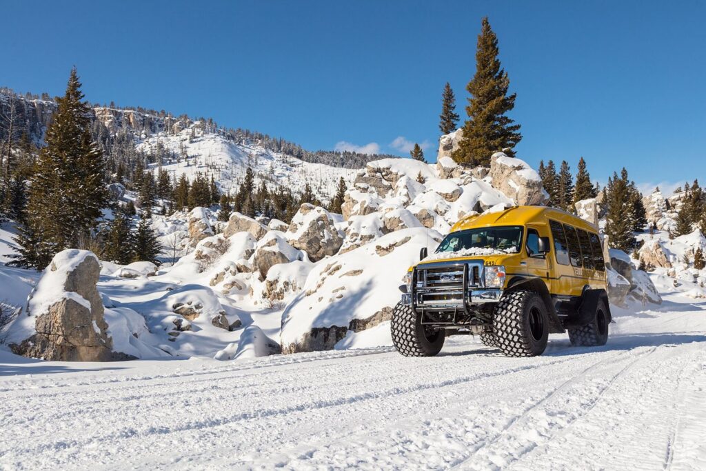 Yellow Yellowstone snowcoach on tracks driving a snowy park road through the Hoodoos near Mammoth