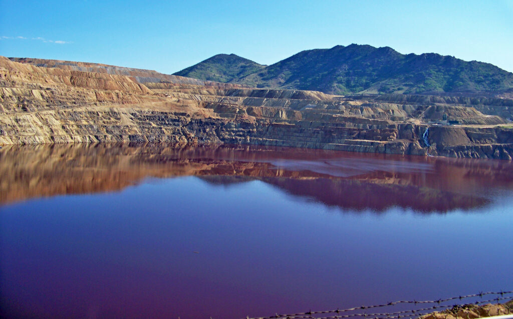 Terraced walls of the Berkeley Pit and its reddish water below the mountains in Butte, Montana