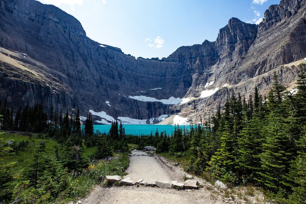 Turquoise Iceberg Lake under steep cliffs at the end of a dirt trail in the Many Glacier valley