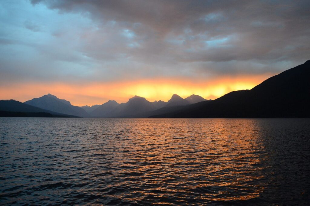 Sunset over Lake McDonald and dark mountain silhouettes seen from Apgar Village in Glacier National Park