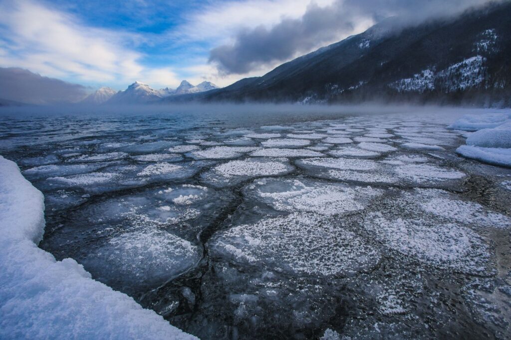 Plates of winter ice on Lake McDonald below snowy mountains and low clouds in Glacier National Park
