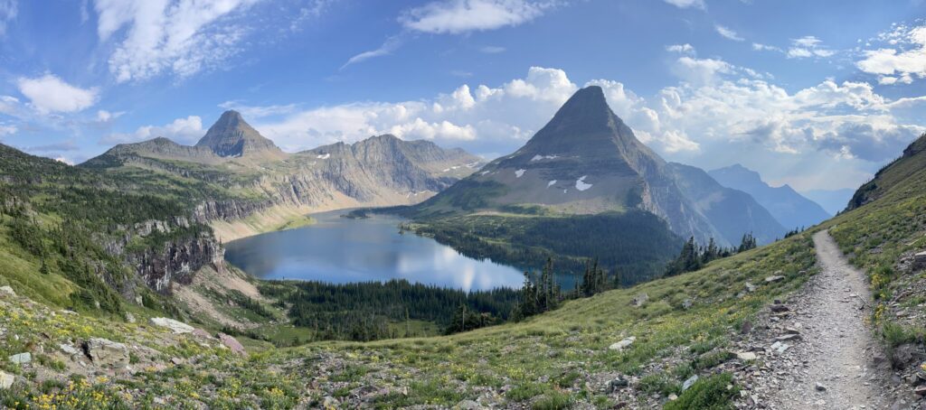 Panorama of Hidden Lake below the pointed summit of Bearhat Mountain, with wildflowers and the Hidden Lake trail curving along the slope at right, near Logan Pass in Glacier National Park